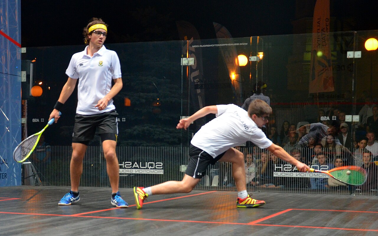 Squash players in a rally on a glass court