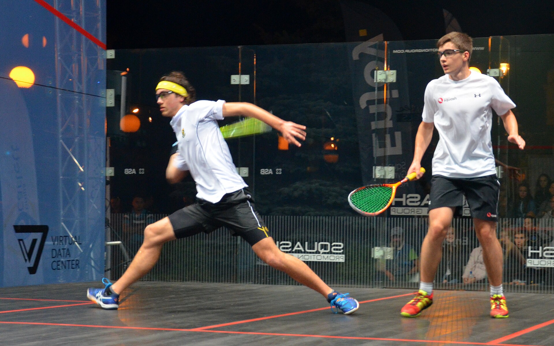 Two players competing on an all-glass championship squash court